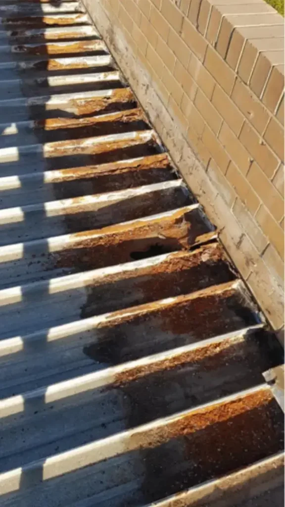 Severely rusted metal roof sheets along a wall showing corrosion and damage, indicating need for roof restoration in Perth