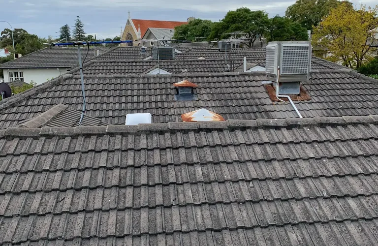 Weathered concrete tile roof in Perth showing ageing tiles and rooftop fixtures before roof tiling or restoration